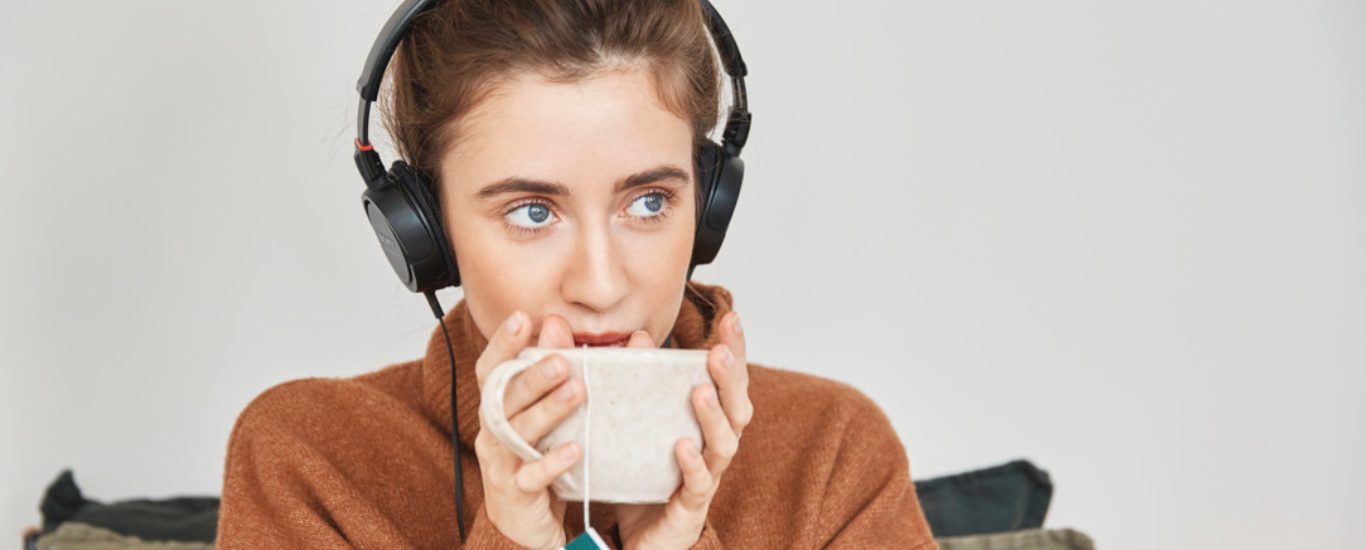 Mujer joven escuchando m&uacute;sica mientras toma t&eacute;